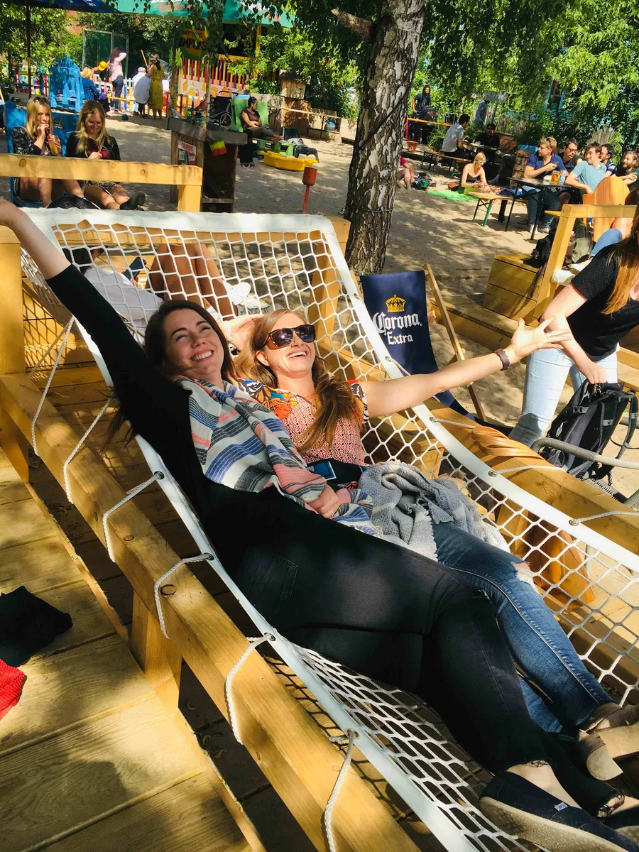 Two Close teammates laughing with their arms stretched out in a big net hammock at a sunny beer garden